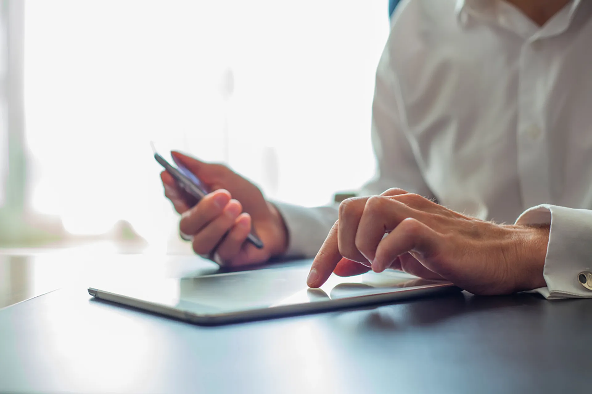 A close-up of a person's hands, holding a smartphone and using a tablet at a desk.